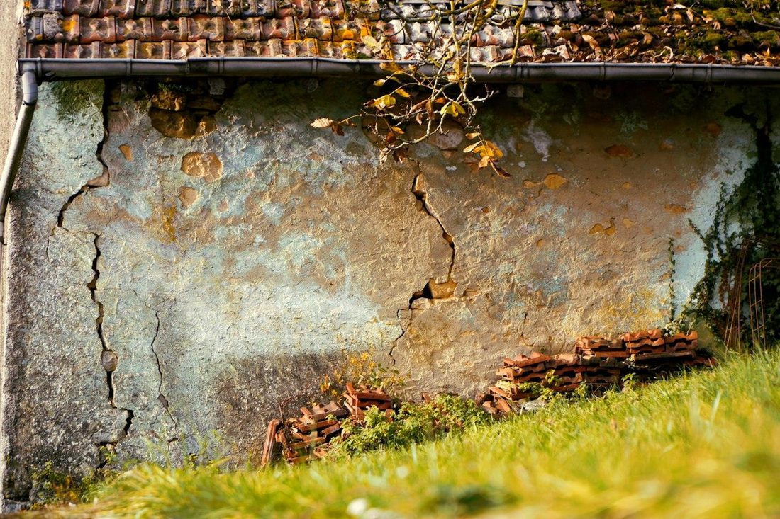 Fissure traversant l'enduit fatigué d'un mur ancien